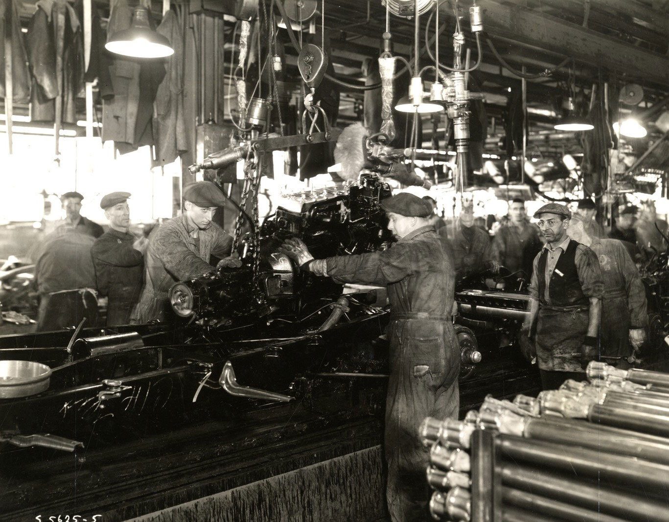 Workers assemble vehicle engines on a factory assembly line.
