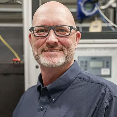 Smiling bald man with beard and glasses, wearing a dark shirt.