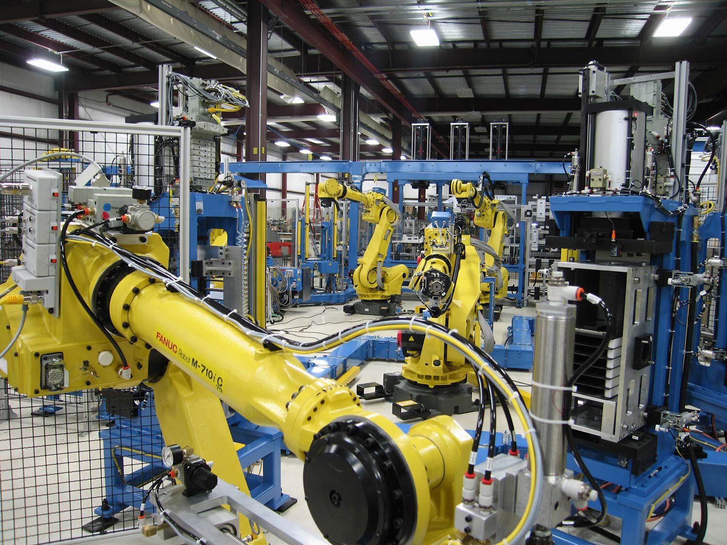 Automated manufacturing facility with numerous yellow Fanuc robots and blue machinery.