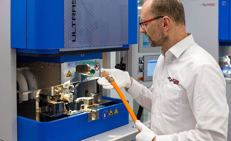 Man in gloves inspecting an orange electrical cable at a blue industrial machine.