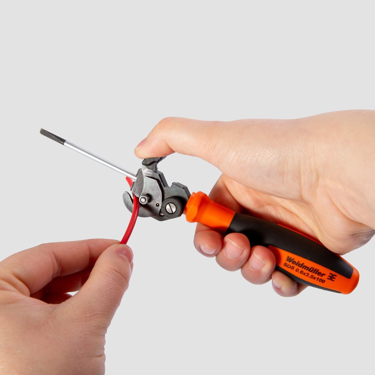Hand using a Weidmüller wire stripper with an integrated screwdriver to remove insulation from a red electrical wire.
