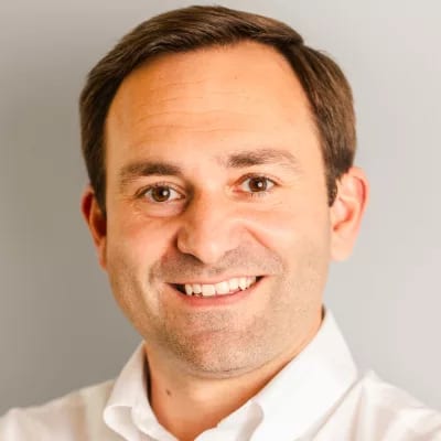 Headshot of a smiling man in a white shirt looking at the camera.