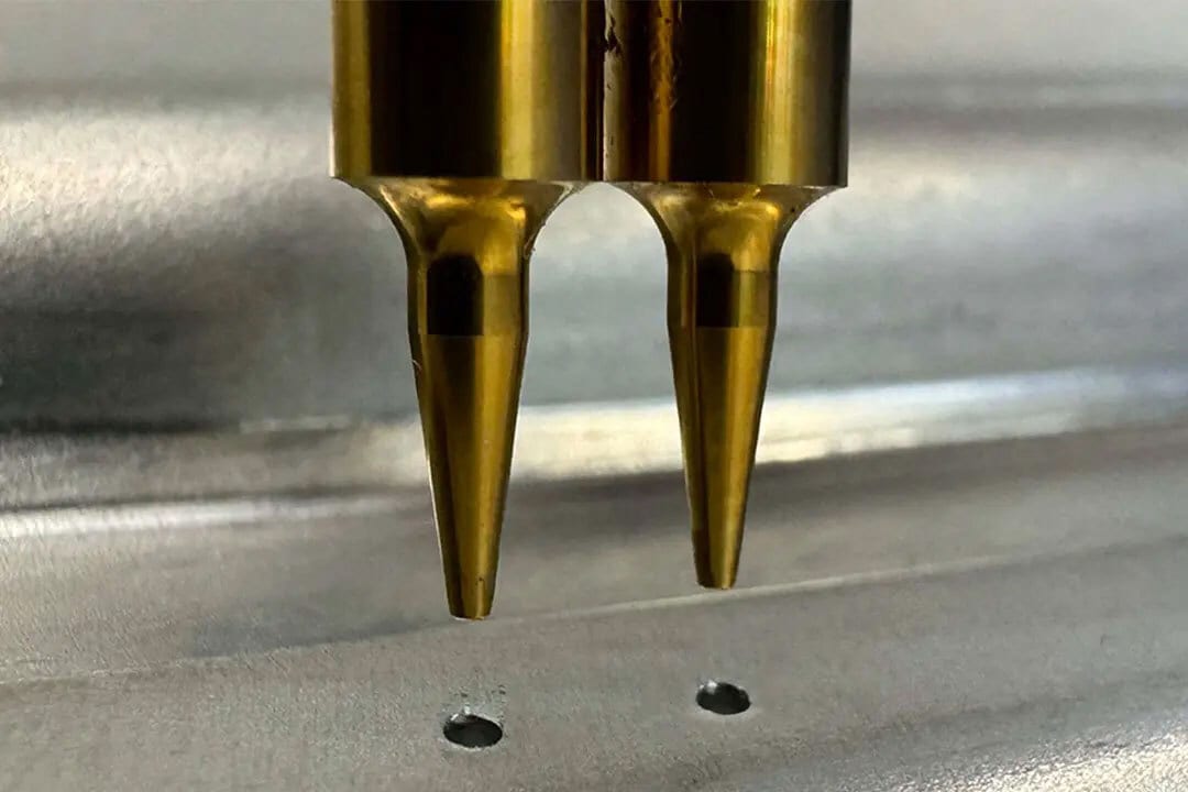 Two golden probes hovering above a metallic surface with two small holes, likely for spot welding or testing.