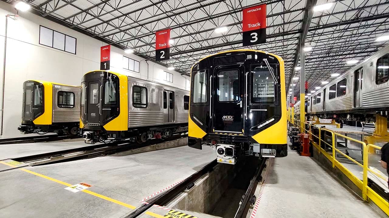 Three black and yellow metro trains in a Hitachi maintenance depot.