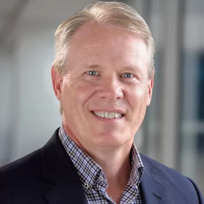 Smiling man with light hair, plaid shirt, and navy blazer.