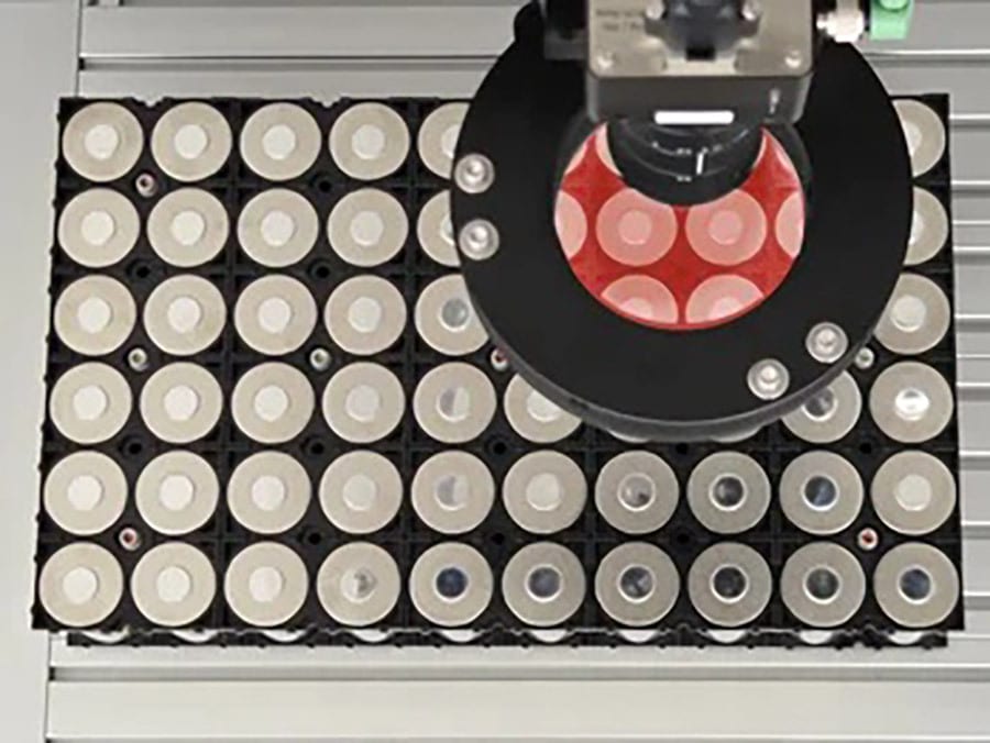 Automated camera with red ring light inspecting circular samples on a grid.
