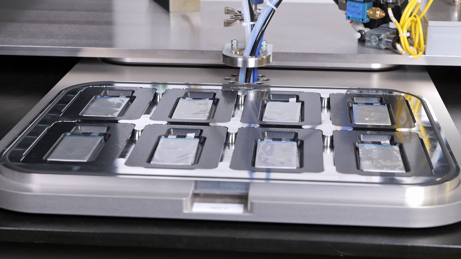 Automated machine working on multiple pouch battery cells in a metal tray.