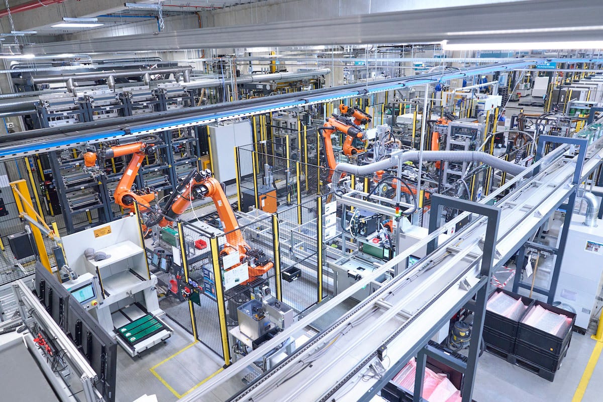 Automated factory with multiple orange robotic arms and extensive conveyor systems.