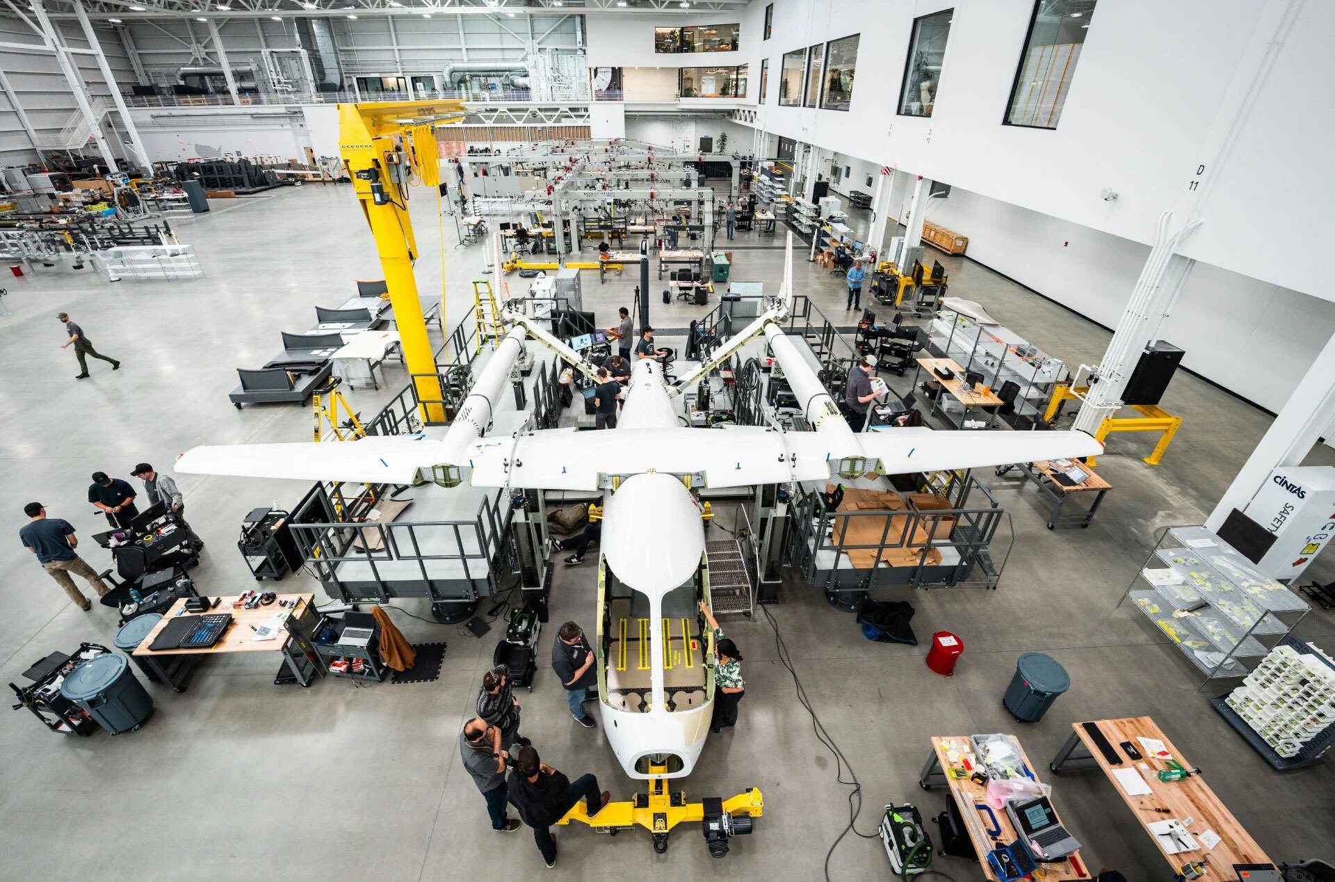 Workers assemble a large white aircraft in a bright factory hangar.