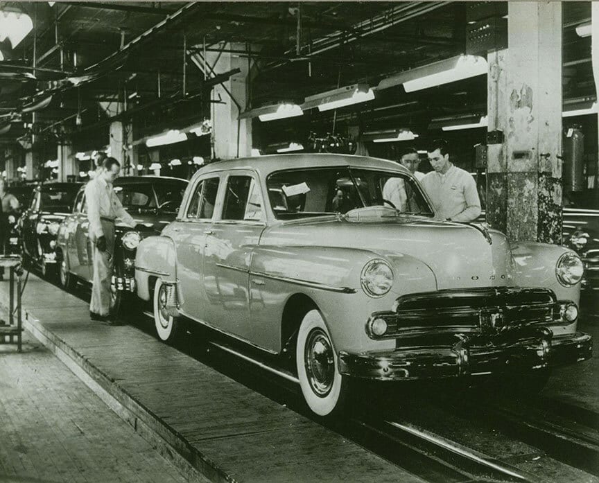 Black and white photo of vintage Dodge cars on an assembly line with workers.