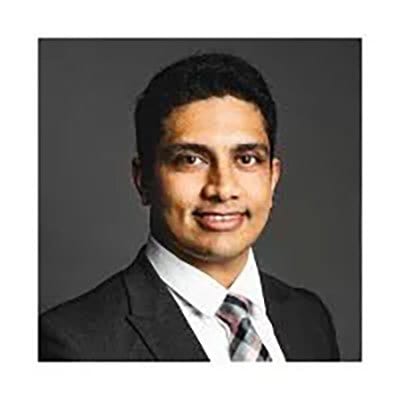Headshot of a smiling man in a suit and tie against a dark background.