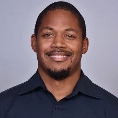 Smiling Black man with a goatee in a dark shirt.