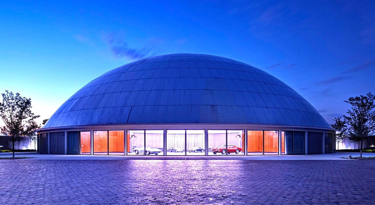 A striking blue domed building under a deep blue sky, showcasing classic cars through illuminated windows.
