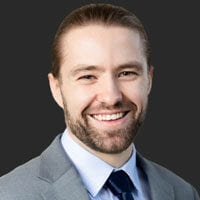 Man smiling with long hair and beard in a suit.