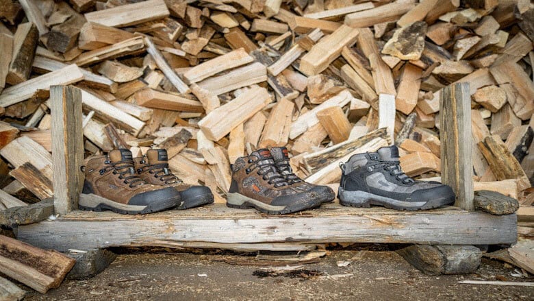 Three pairs of boots on a wooden stand, with a background of stacked firewood.