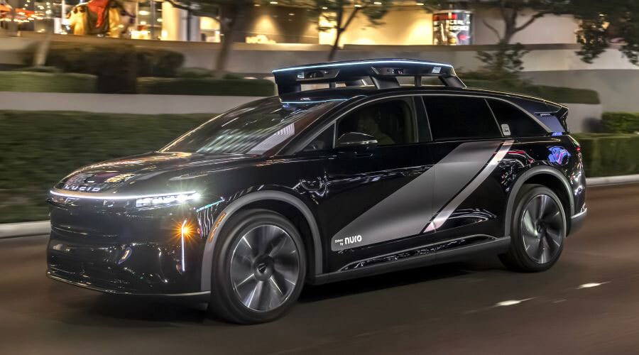 Black Lucid Air autonomous vehicle with Nuro sensors & branding, driving at night.