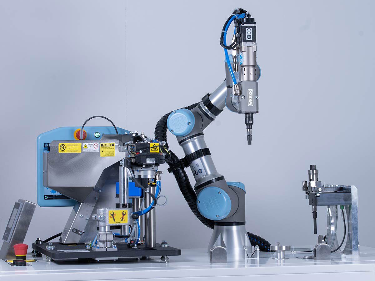 Robotic arm with an automated screwdriver tool, next to an automated parts feeder.
