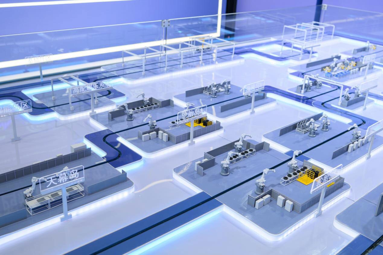 A detailed miniature model of an automated factory floor with robotic arms, conveyor belts, and illuminated production zones.