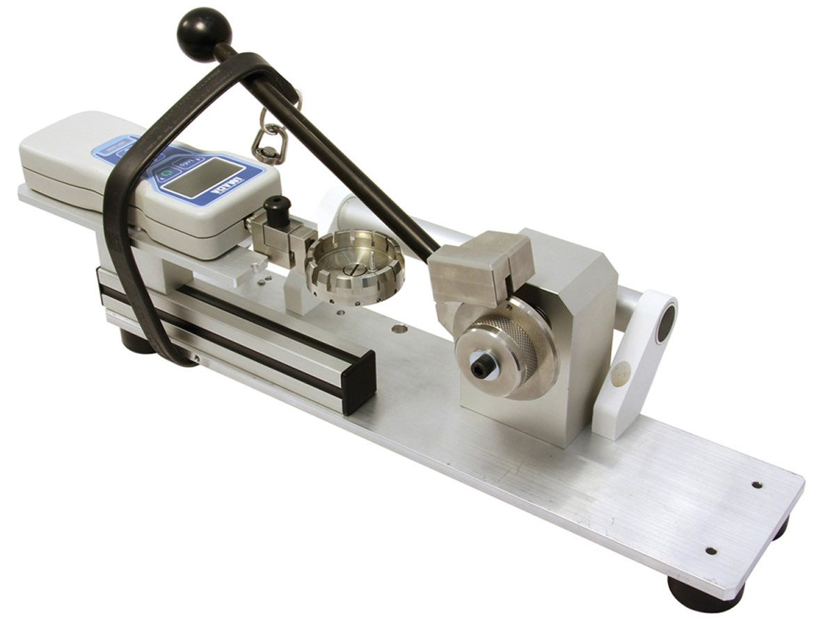A laboratory instrument featuring a digital gauge, a black lever, and various metal testing components.