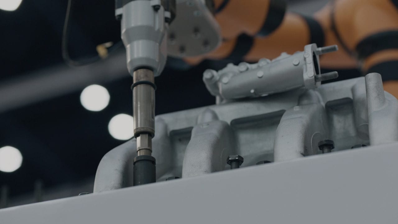 A robotic arm's tool working on an engine manifold in an industrial setting.