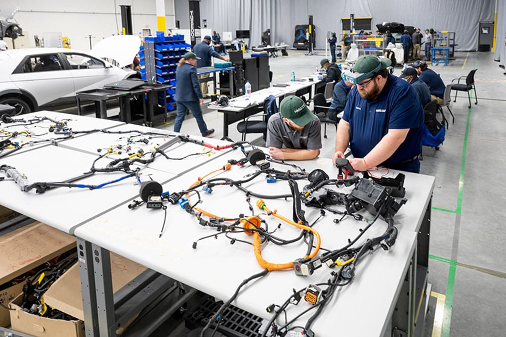 Factory workers assembling intricate vehicle wiring harnesses on large tables.