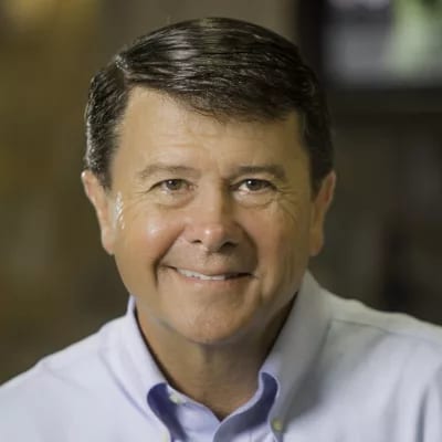 Smiling middle-aged man in a light blue collared shirt looking directly at the camera.