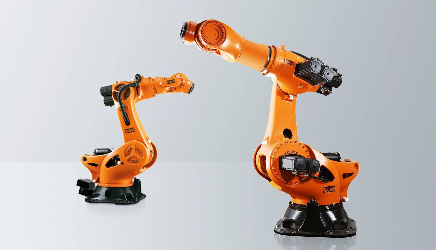 Two KUKA orange industrial robots, one smaller and one larger, on a light grey background.