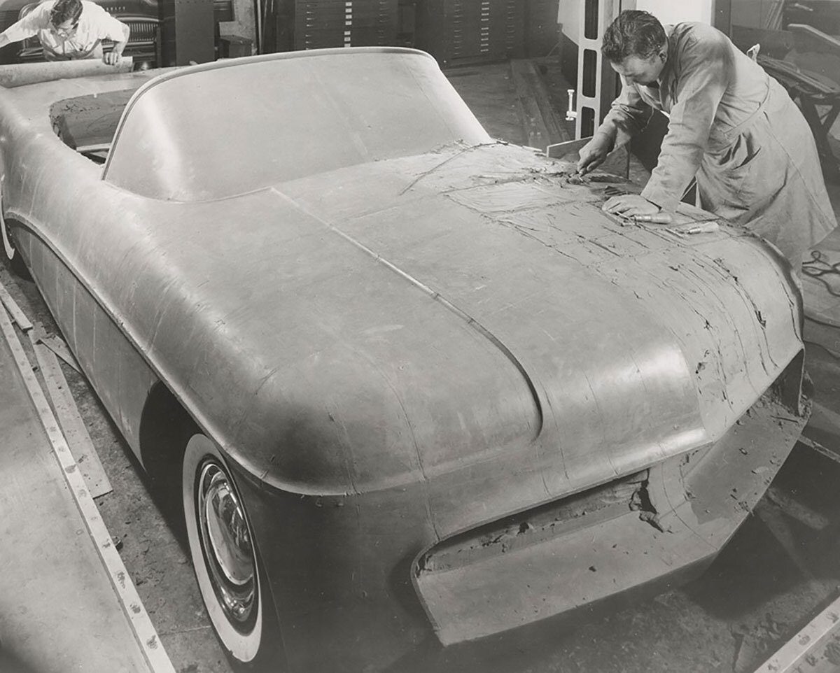Two men sculpt a clay model of a car, likely a prototype, showcasing the detailed design process.