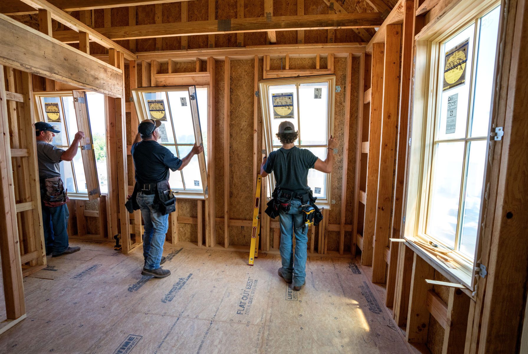 Three construction workers installing windows in a wooden house frame.