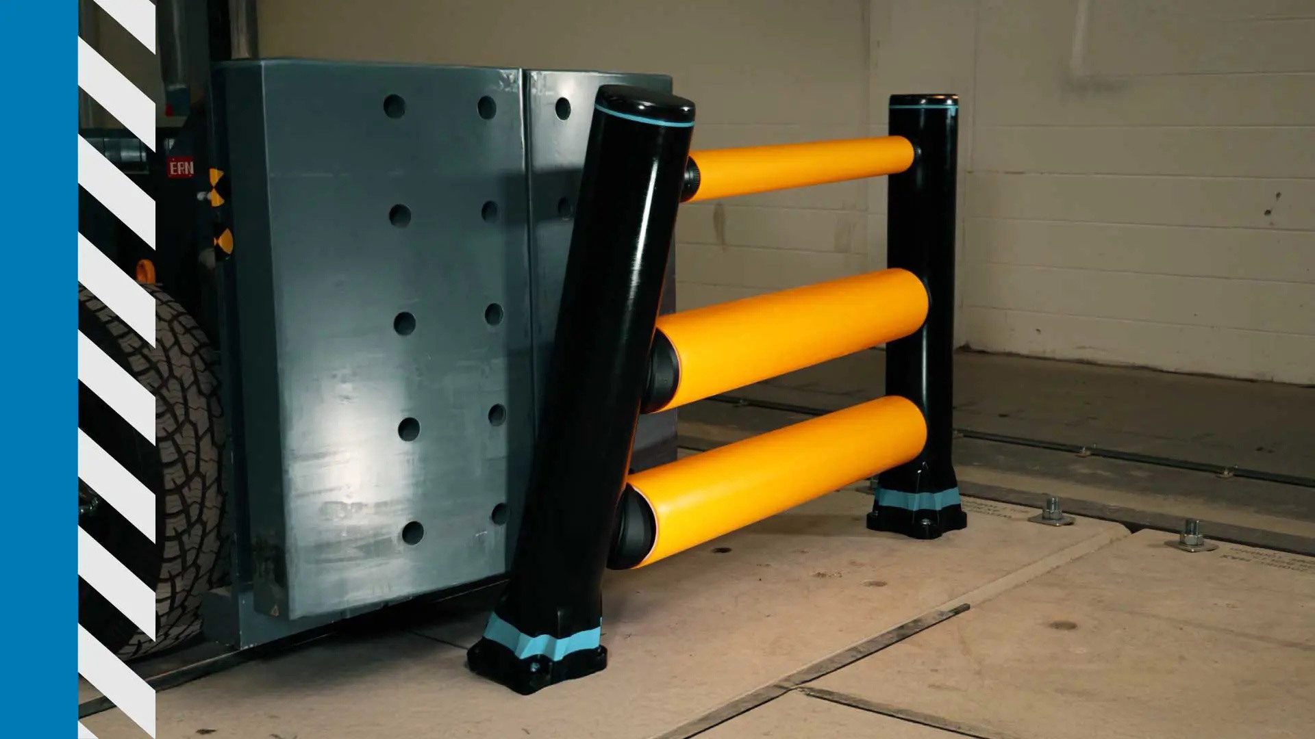 A yellow and black industrial barrier in front of a large grey machine with a tire, on a concrete floor.