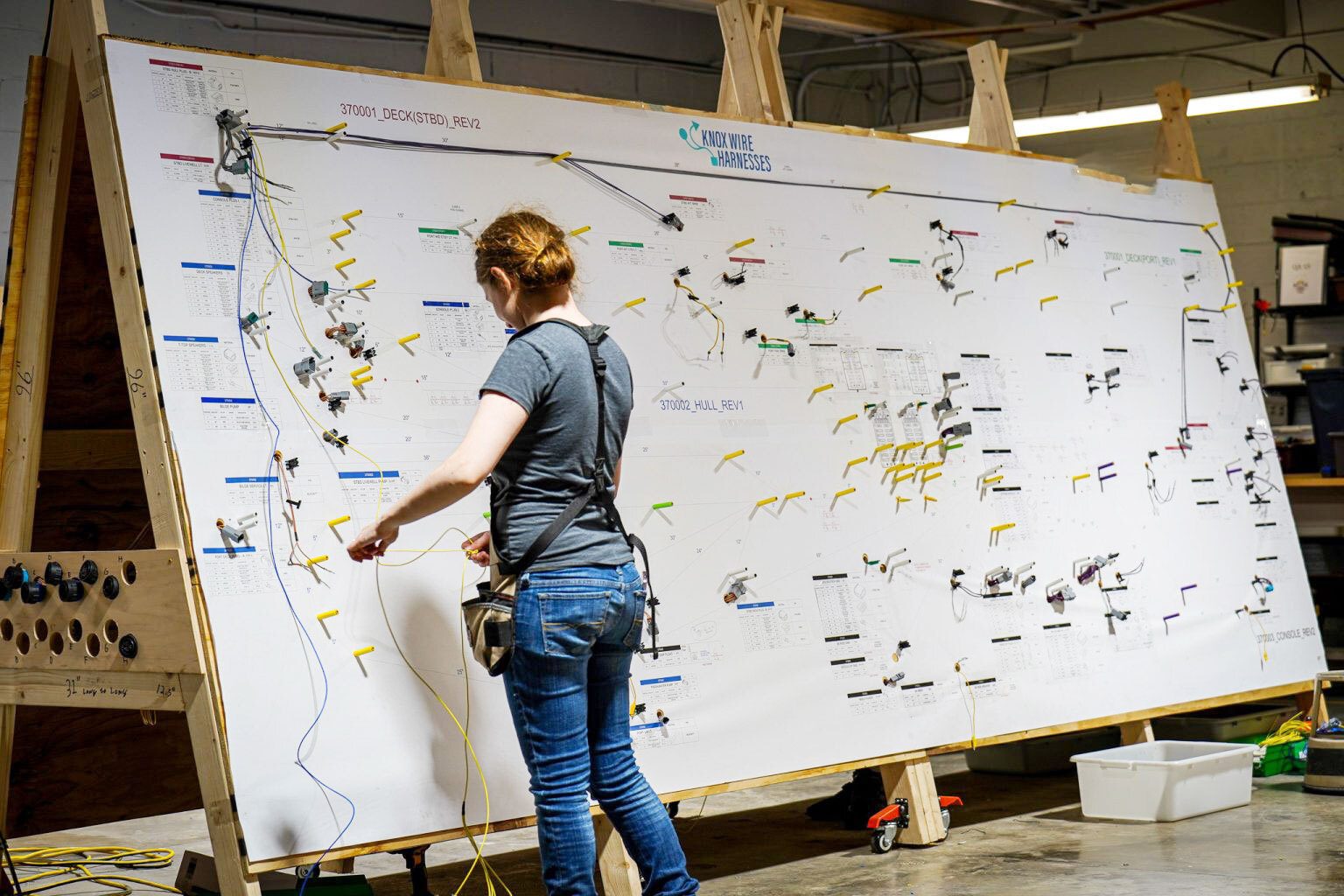 A woman works on a large diagram board, assembling a complex wire harness for Knox Wire Harnesses.