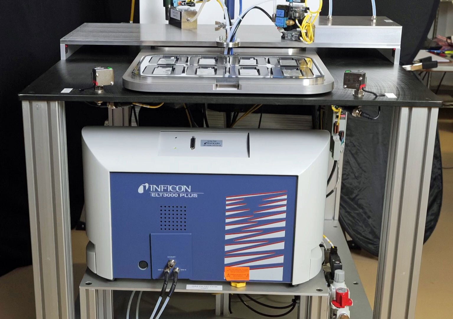 Industrial INFICON ELT3000 PLUS leak detector on a rack with a sample tray.