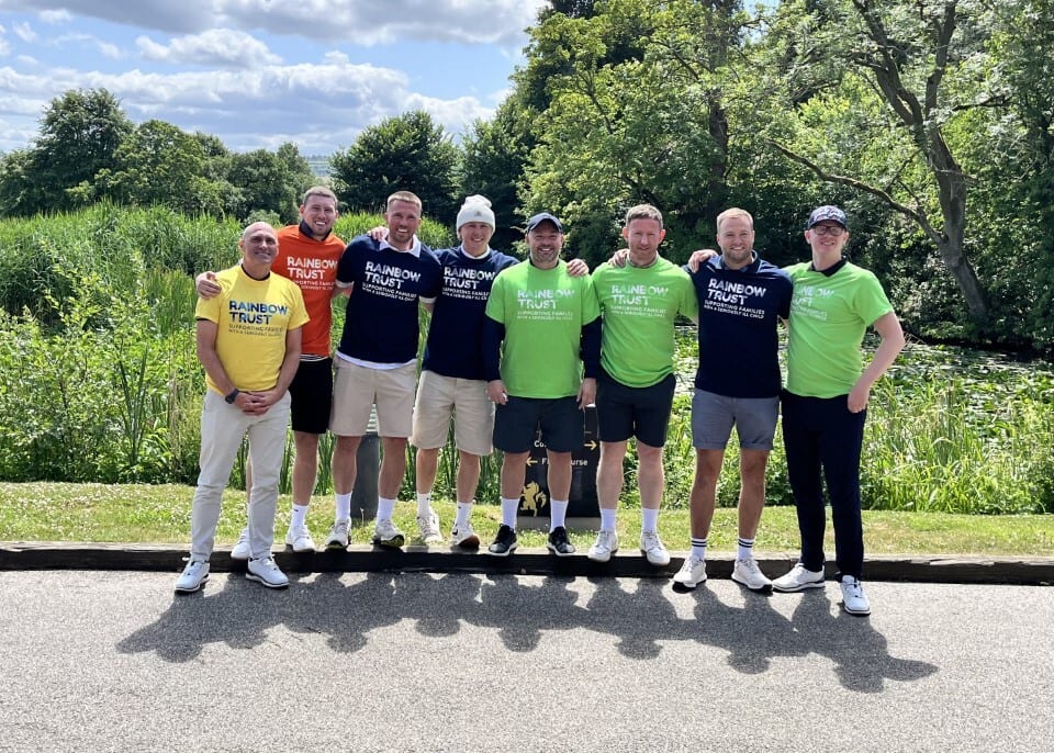 Group of men wearing "Rainbow Trust" t-shirts pose outdoors.