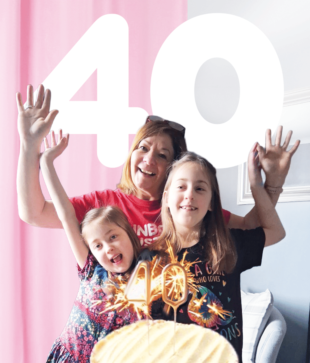 Woman celebrating 40th birthday with two young girls, cake, and sparklers, with a large '40' behind.