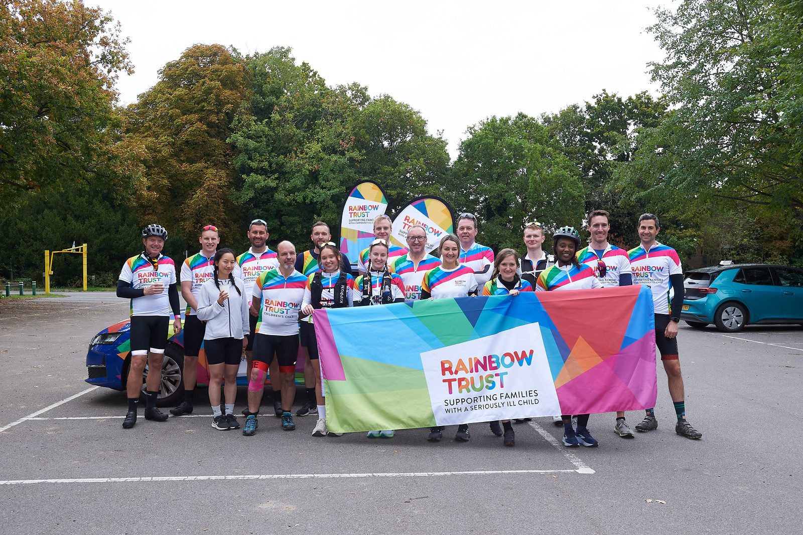 Rainbow Trust cycling team holding a banner supporting families of seriously ill children.