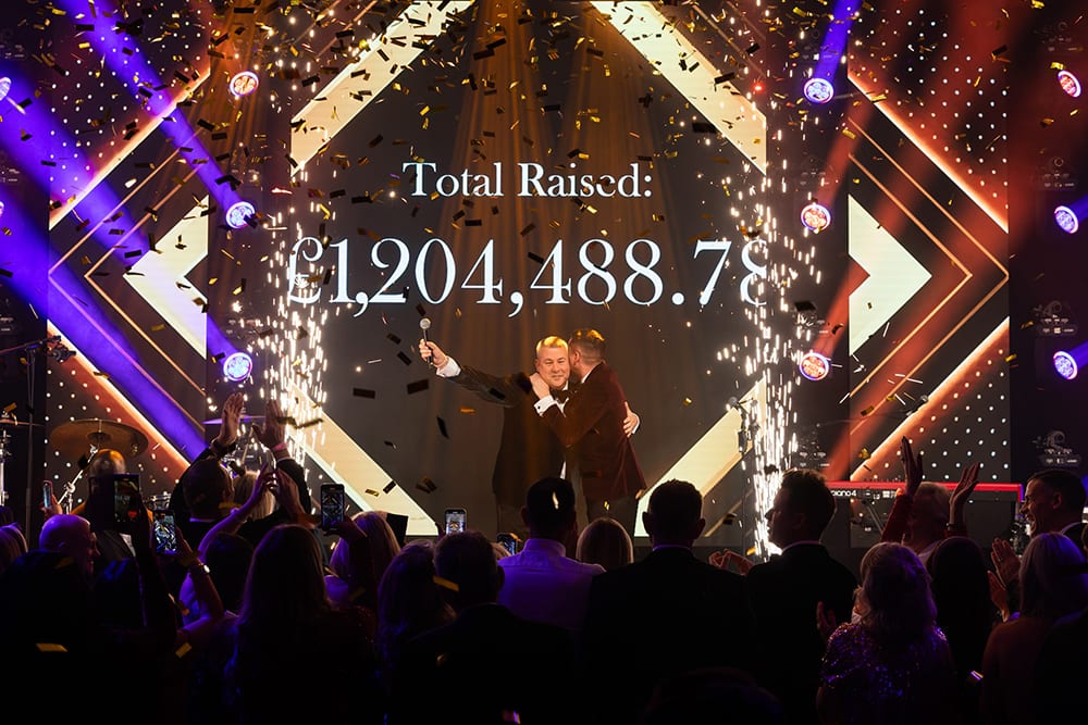 Men on stage celebrating £1.2M raised, with confetti and pyrotechnics.