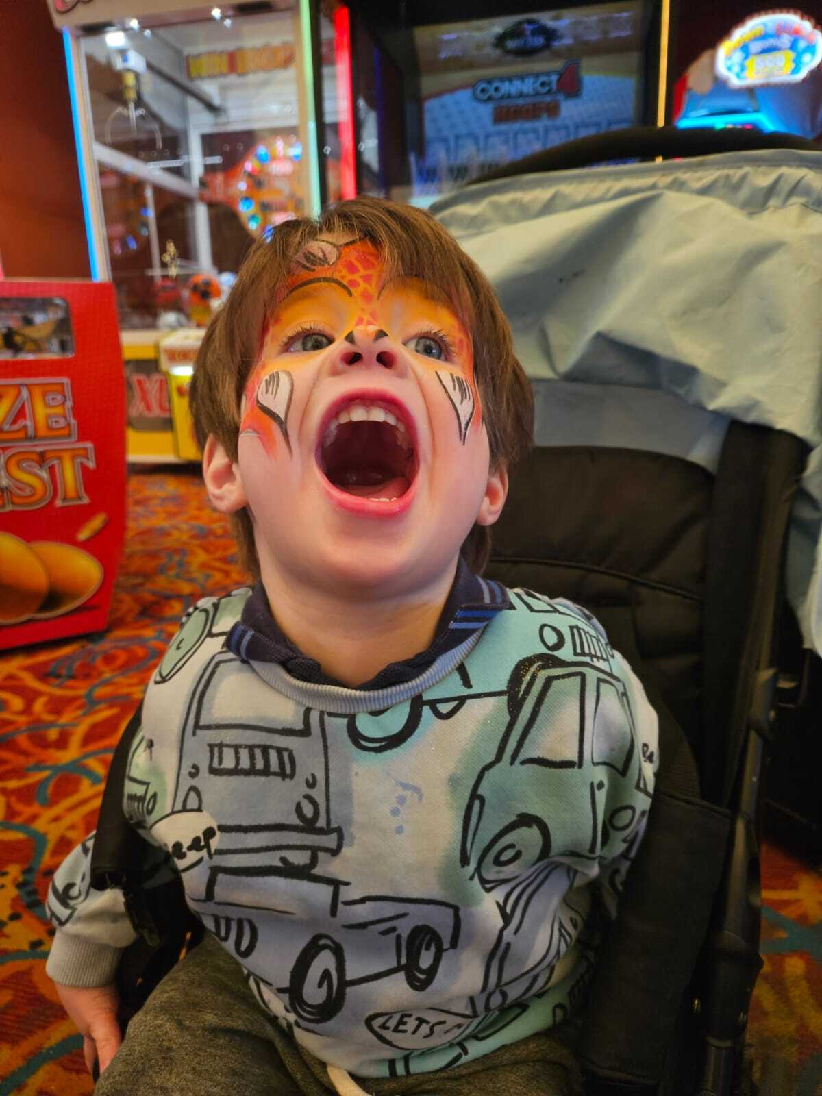 Child with animal face paint roaring in a stroller at an arcade.