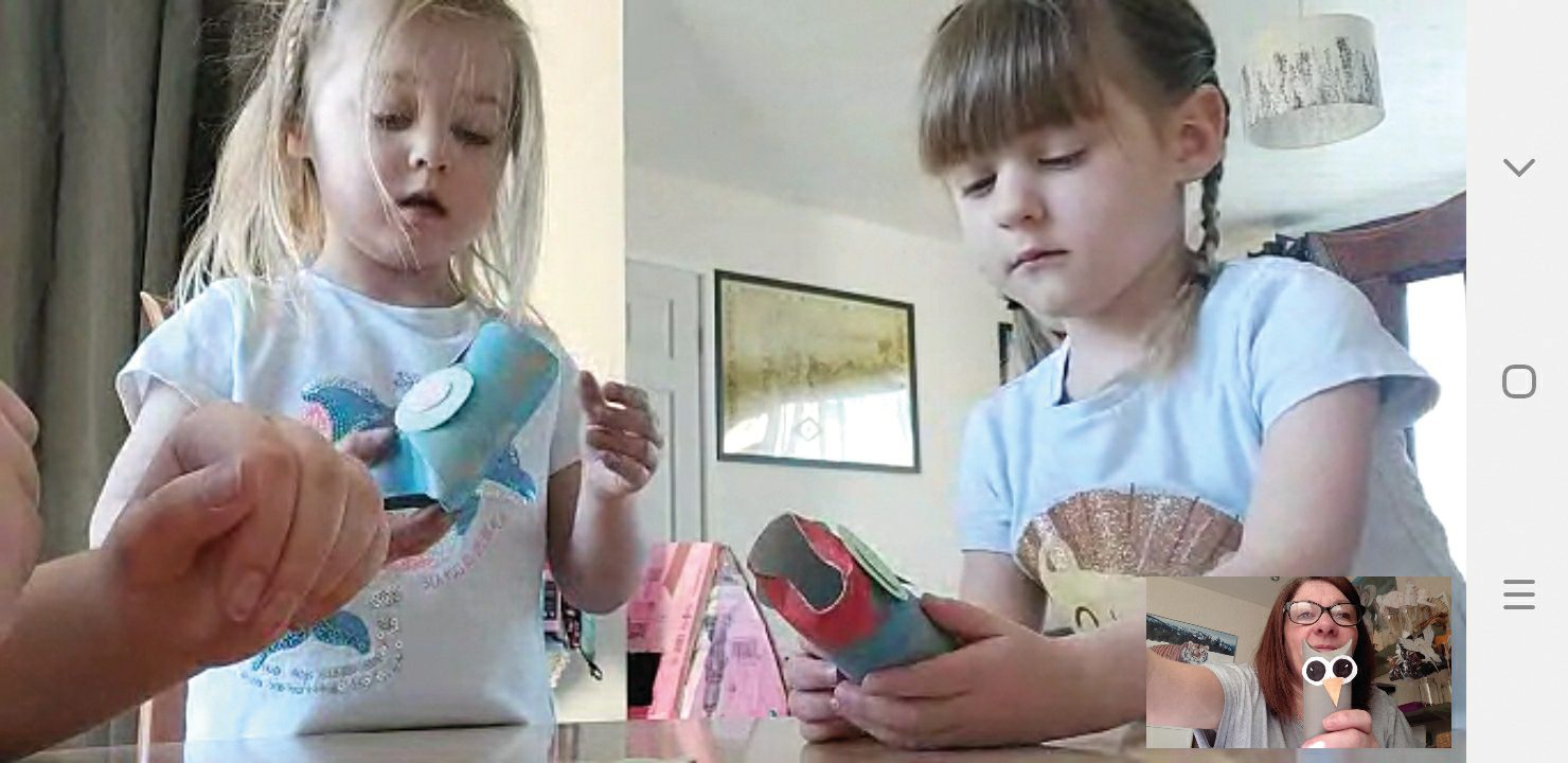 Two young girls doing crafts during a video call, each holding their creations.
