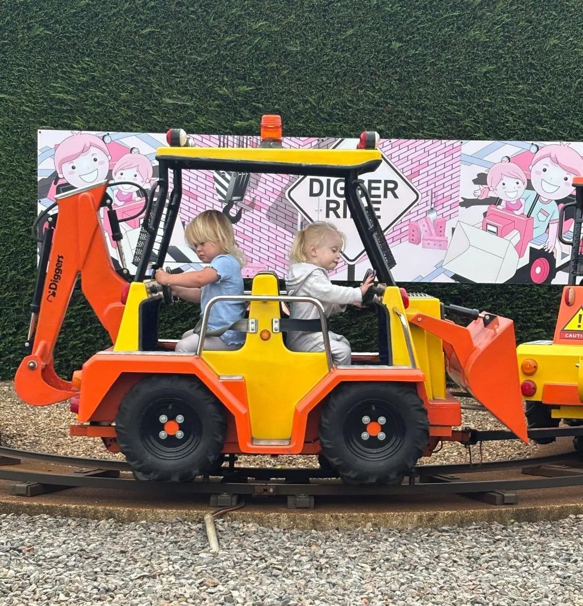Two toddlers on a digger-themed amusement park ride.