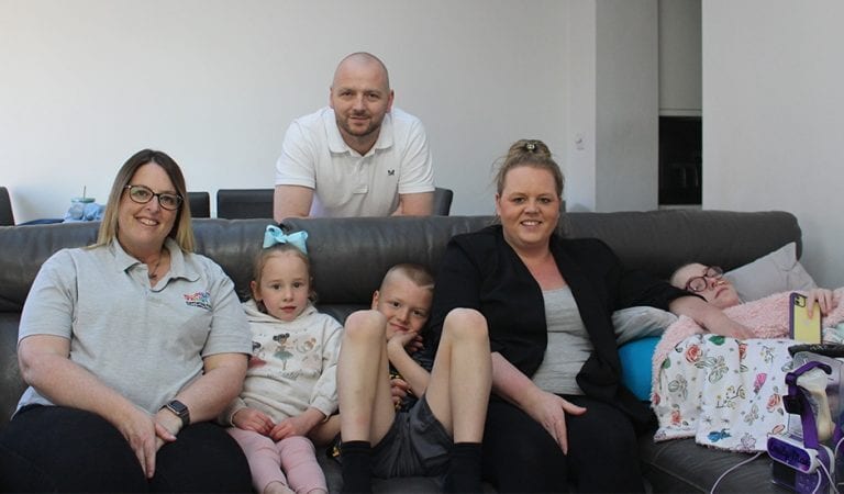 A family of six, including adults and children, seated and reclining on a dark sofa.