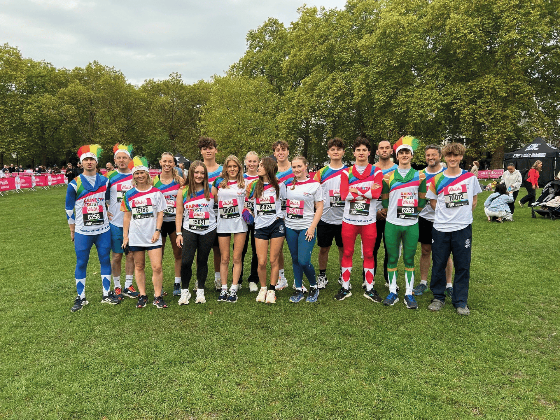 Cheerful runners in Rainbow Trust gear and costumes pose on a grassy field after a race.