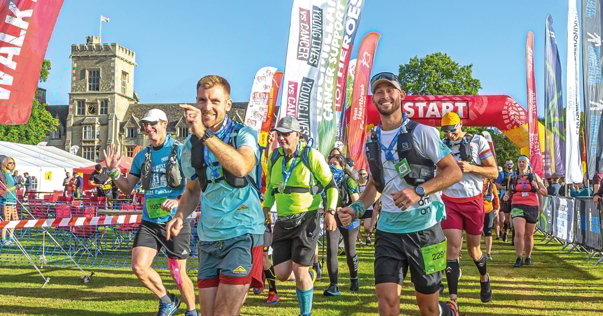 Smiling runners at the start of a charity race, surrounded by event banners and a historic building.