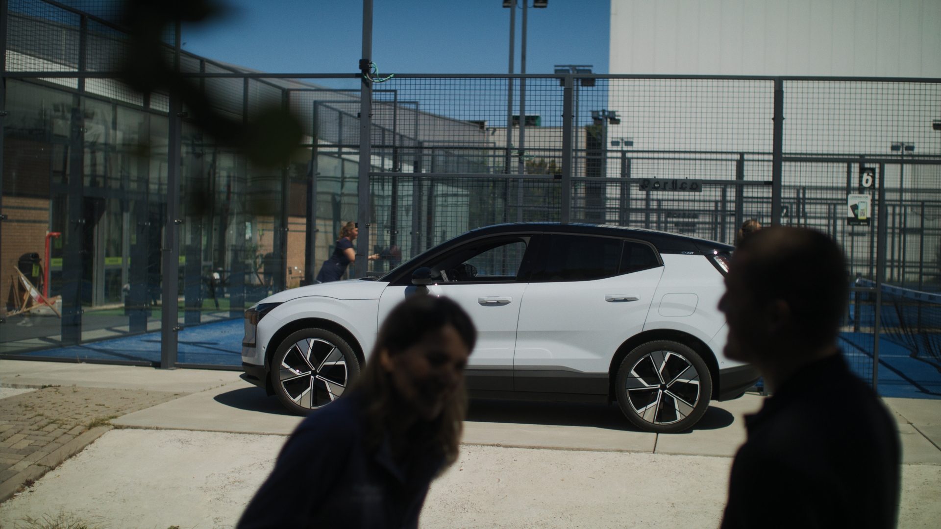 White electric hatchback parked by outdoor padel courts.