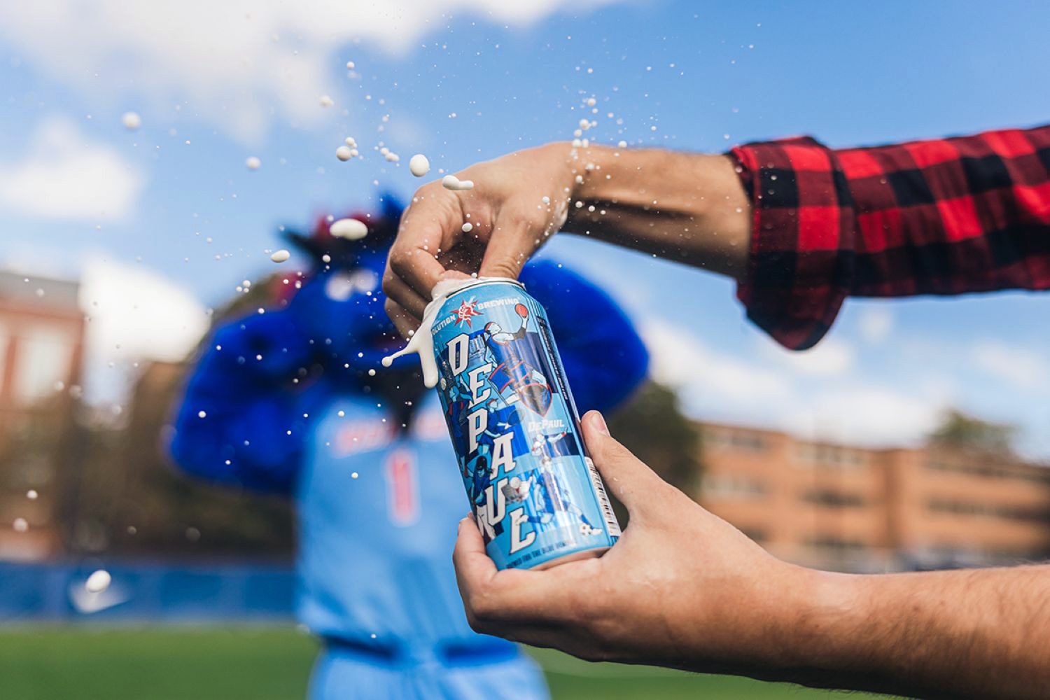 Hand opening DePaul-branded Revolution beer can with DePaul mascot in background