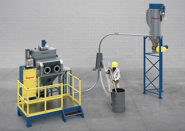 Industrial setup: worker uses a vacuum hose to transfer material between processing equipment and a drum.