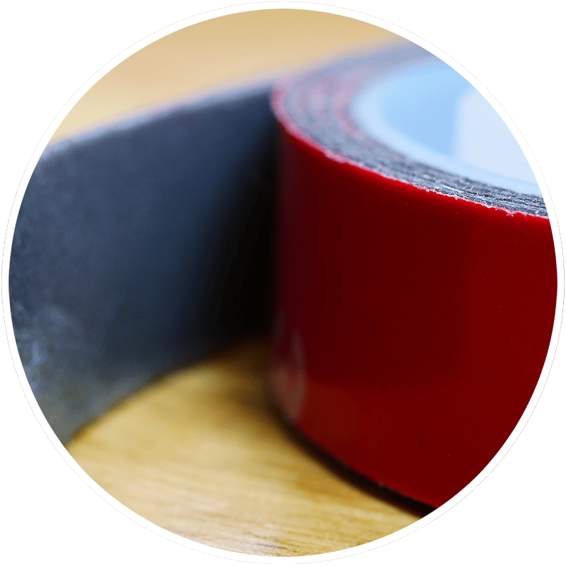 Close-up of a roll of red and black double-sided tape on wood.