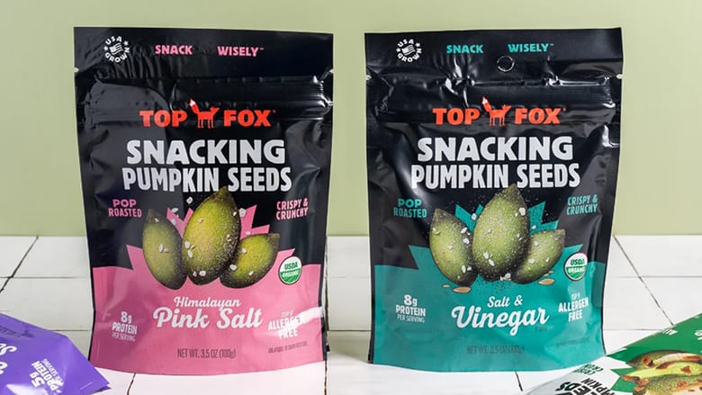 Pair of Top Fox pumpkin seed packages on table with flattened packages beneath them.