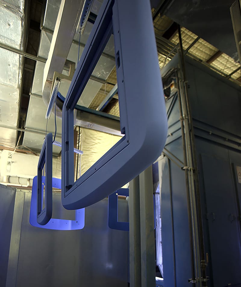 Light blue metal frames on a conveyor system in an industrial paint or coating facility.