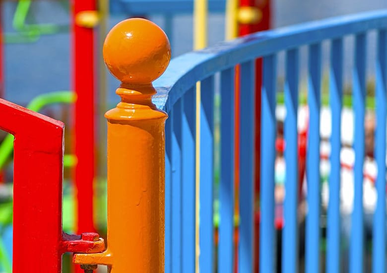 Vibrant orange post with a spherical top, connected to red and blue playground railings.