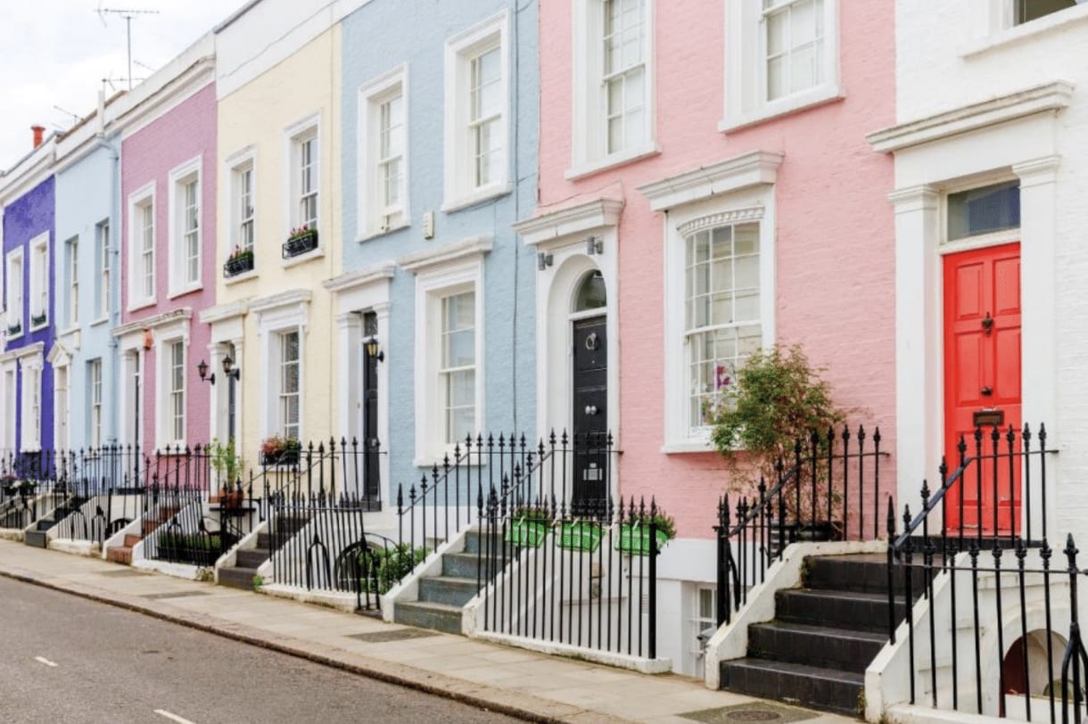 A street lined with colorful pastel houses, white windows, steps, and black railings.